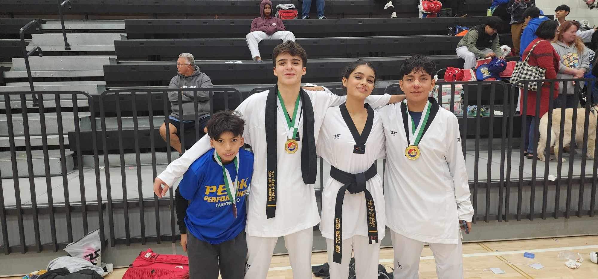 one female and 3 male tennagers  celebratig after a taekwondo tournament